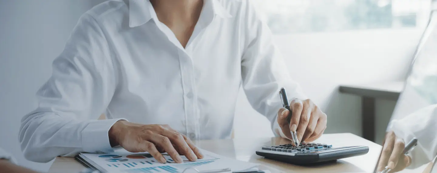 Moteris su baltais marškiniais naudojasi skaičiuotuvu, pildo finansus